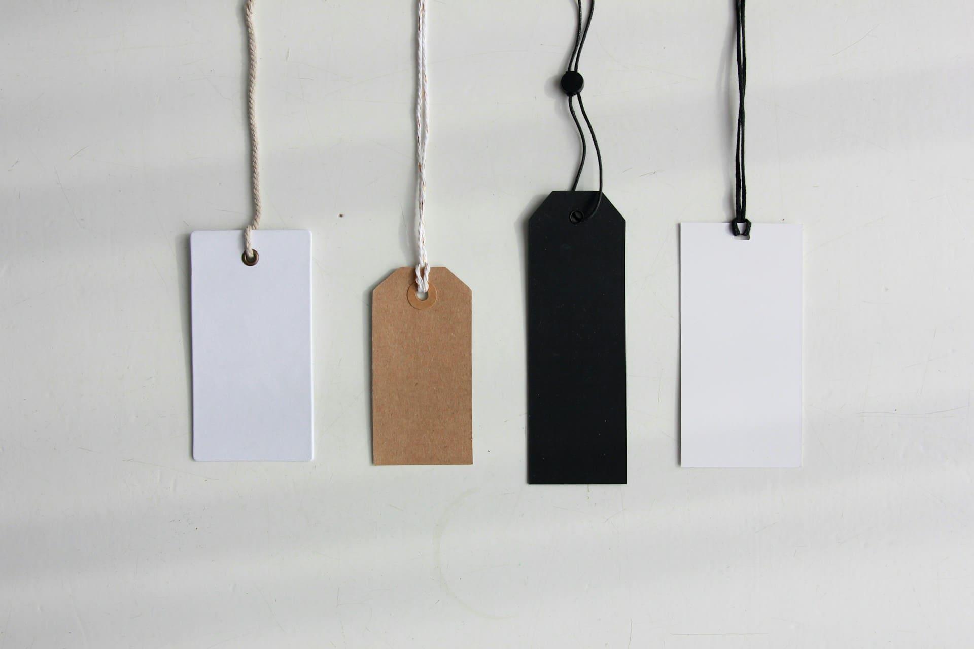 Four distinct tags of varying shapes and colors hanging on a textured wall, showcasing different designs and styles.