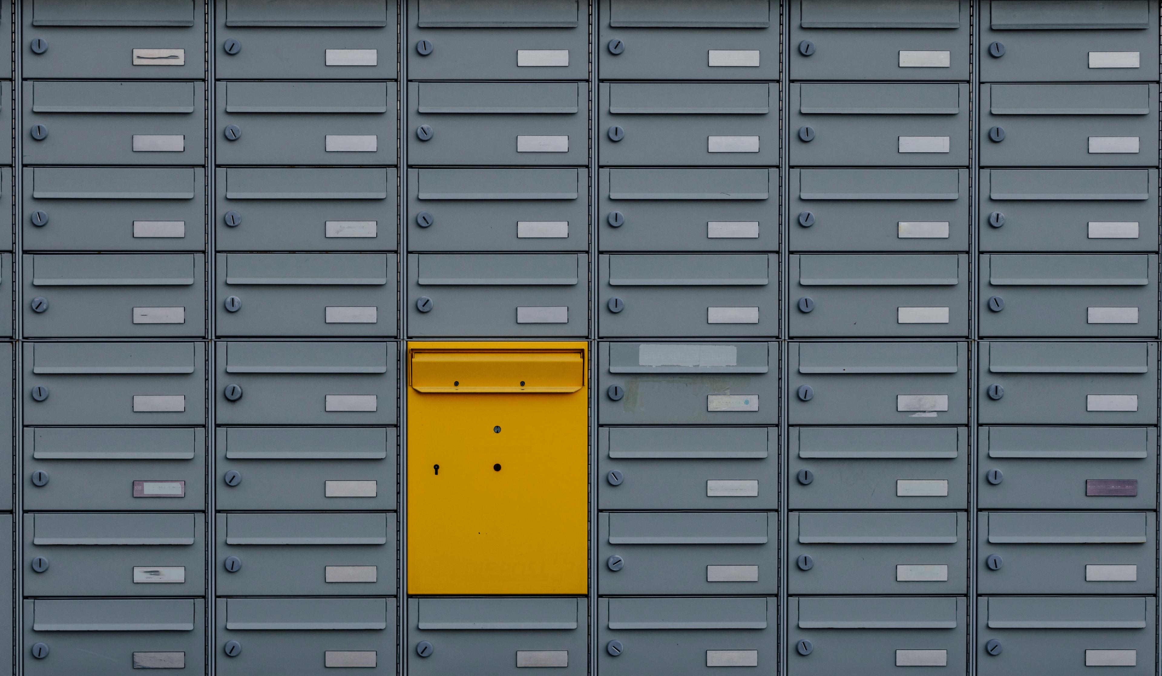 A bright yellow door stands in front of a large cluster of mailboxes, creating a vibrant and inviting scene.