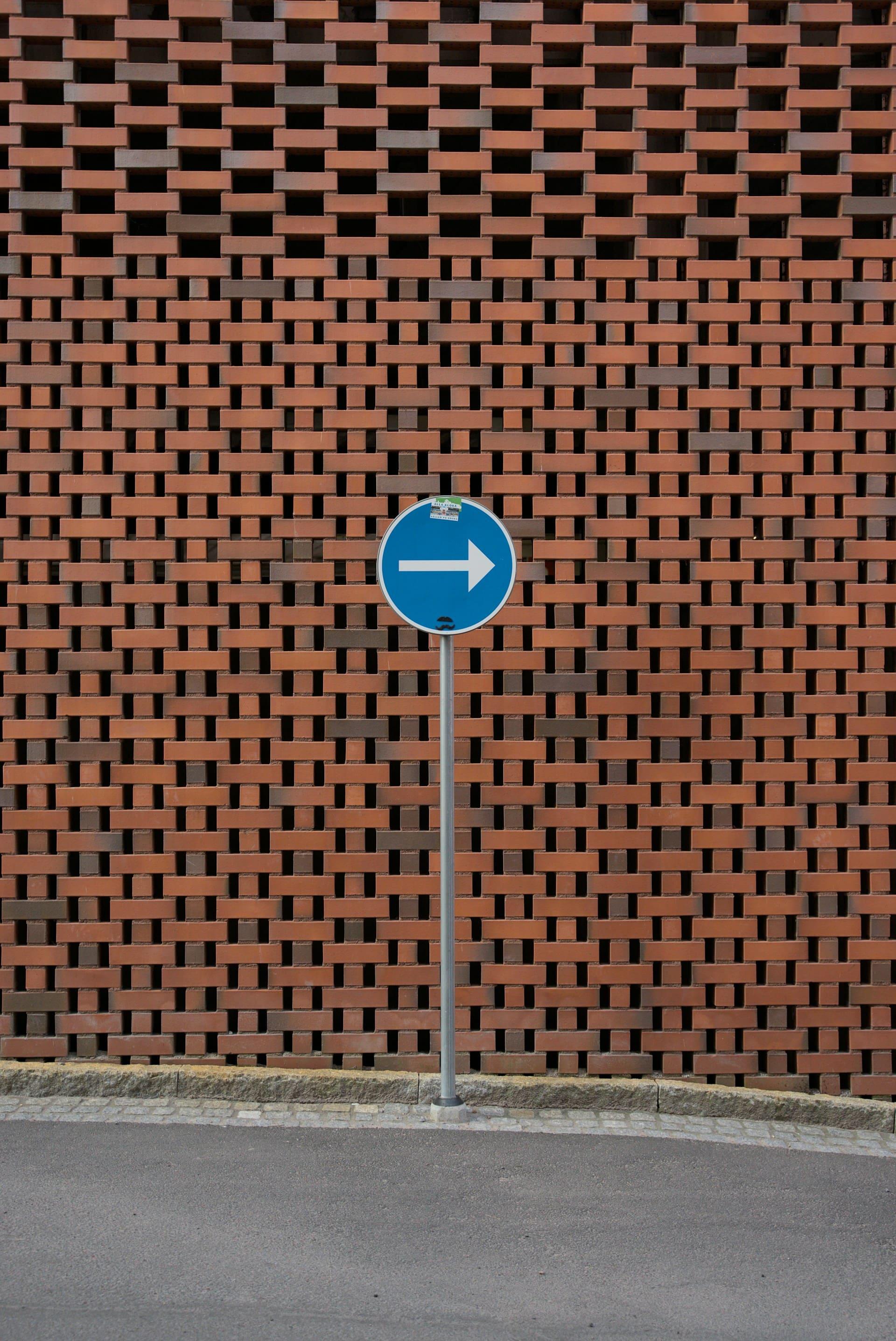 A street sign stands in front of a textured brick wall, providing directional information in an urban setting.