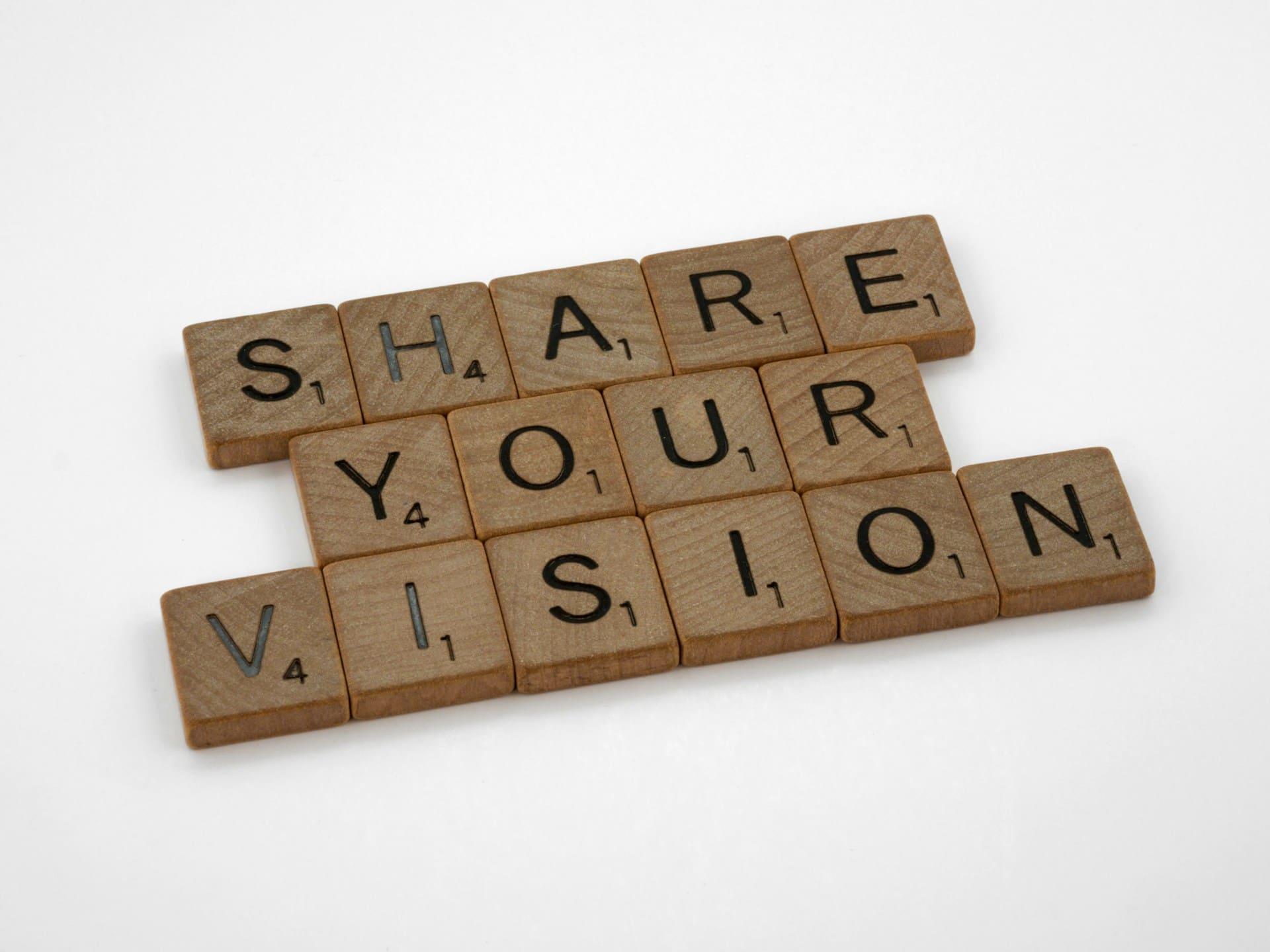 Wooden scrabble blocks arranged to spell "Share Your Vision" on a textured surface, emphasizing creativity and inspiration.