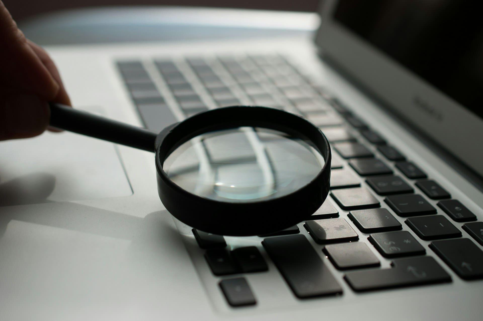 A person using a magnifying glass to search for information on a laptop screen.
